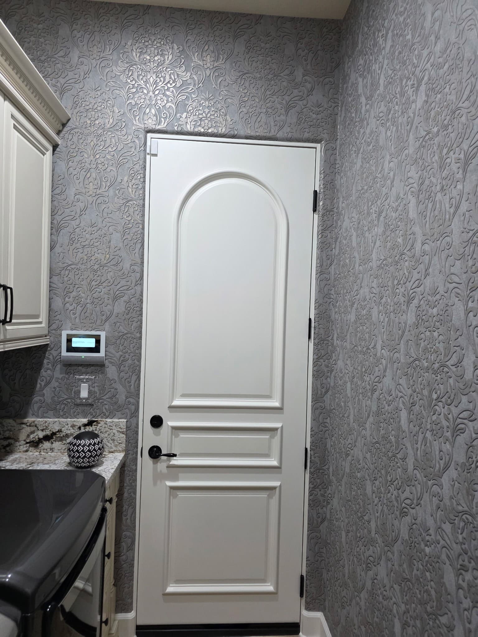 Laundry room with silver embossed damask wallpaper surrounding a white arched door