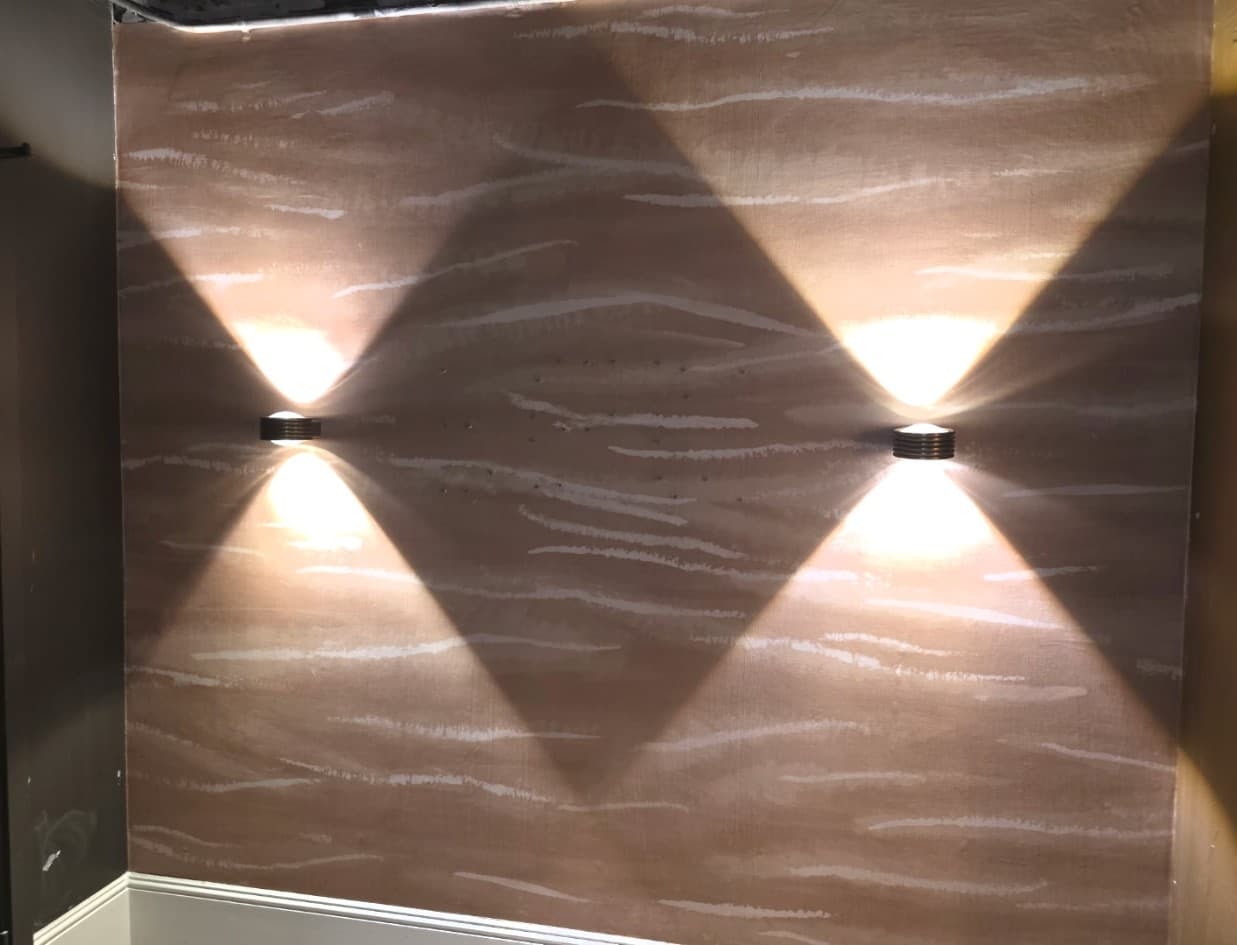 Bronze wavy textured wallpaper dramatically lit by two wall sconces