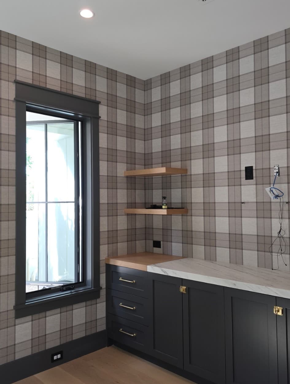 Plaid tartan wallpaper in a laundry room with dark navy cabinets and open shelving