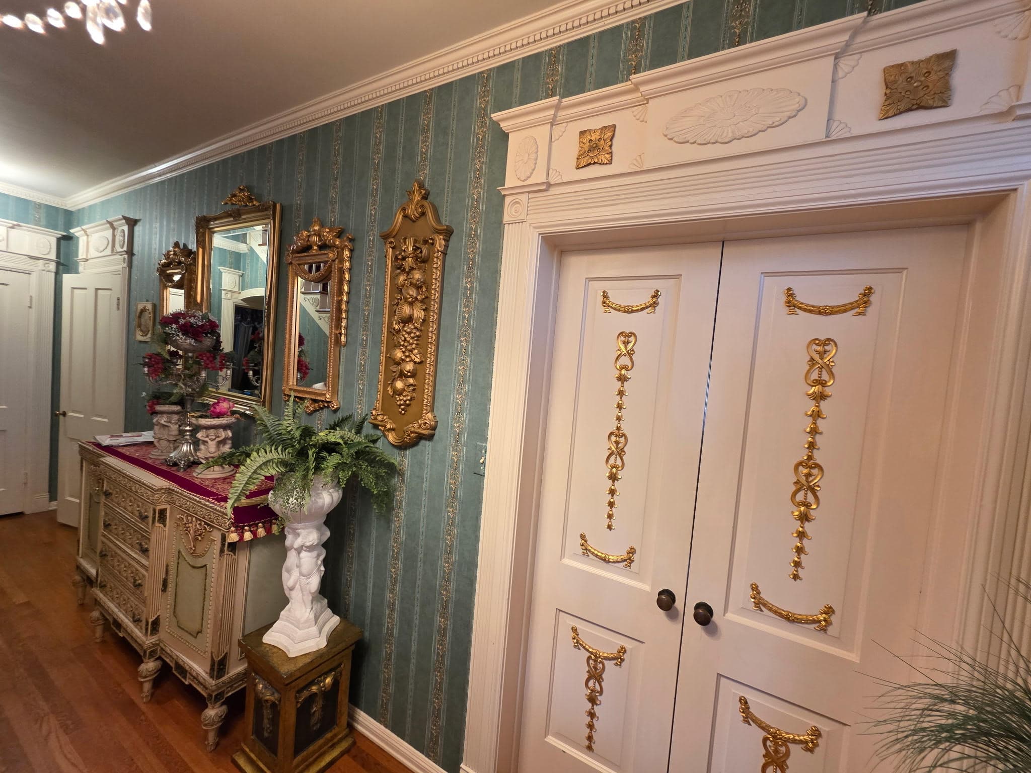 Luxury foyer with teal wallpaper, ornate gold mirrors and white decorative door